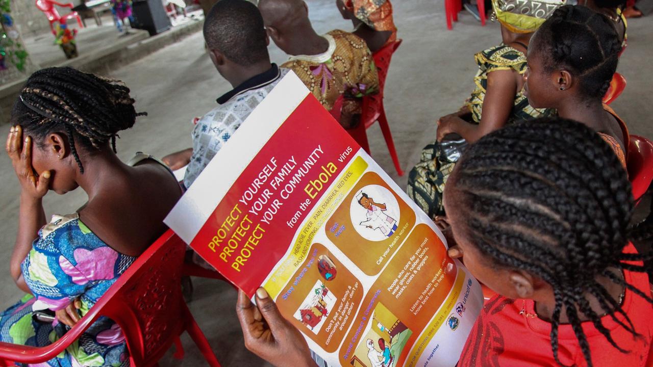 Frauen in Liberia sitzen auf Plastikstühlen und lesen Informationsblätter über den Schutz vor dem Ebola-Virus