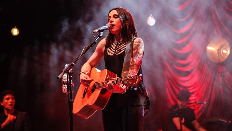 Amy Macdonald steht auf der Bühne spielt auf der umgehängten Gitarre und singt ins Mikrofon