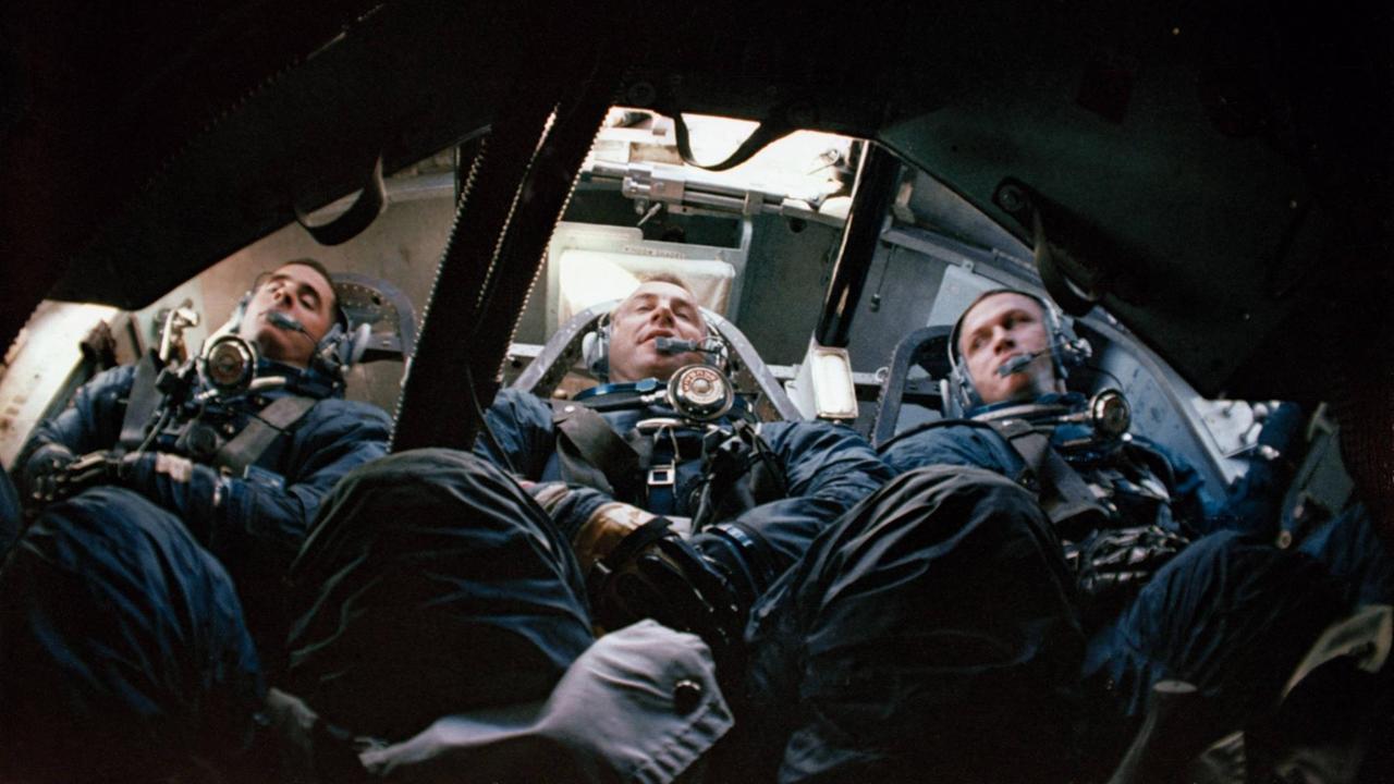 Drei Astronauten, auf dem Rücken liegend und festgeschnallt, in einer Raumkapsel
