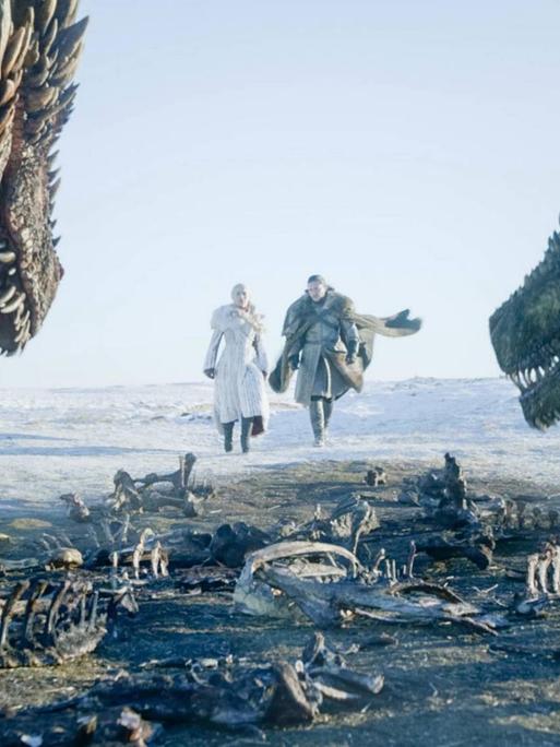 Im Vordergrund Skelette von Dinosauriern. Vom Seitenrand ragen zwei Dinosaurierköpfe ins Bild. In der Mitte sind die beiden Darsteller zu sehen wie sie durch eine Landschaft laufen.