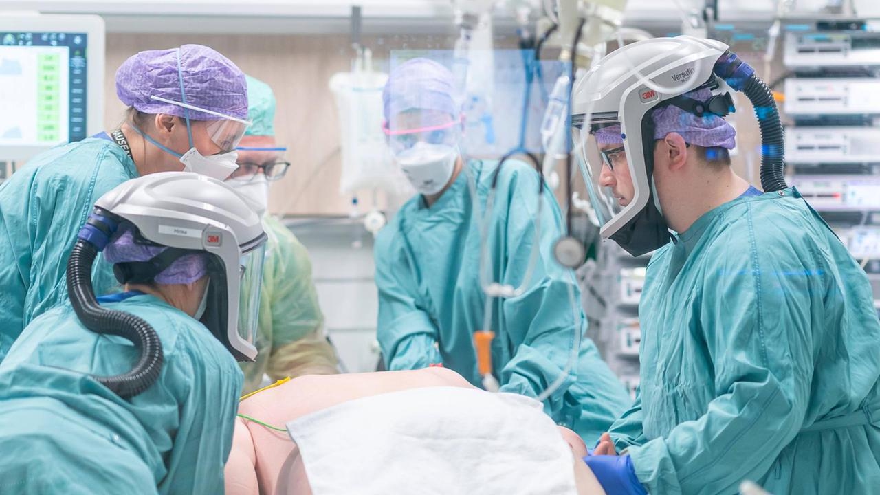 Auf einer Intensivstation stehen Ärzte und Pfleger in mit Schutzmasken am Bett eines Covid-Intensivpatienten.