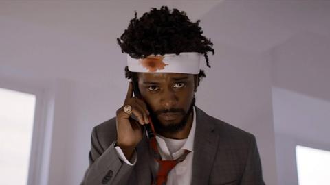 Ein schwarzer Mann mit einem blutigen Verband am Kopf und einem Handy am Ohr.