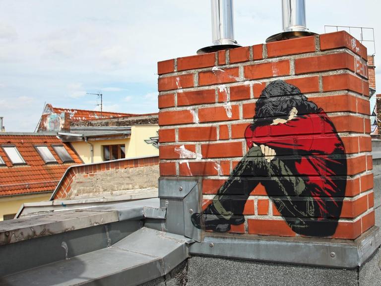 Ein Bild des Street-Art-Künstlers "Alias" auf einem Schornstein auf einem Dach - ein Junge, der sein Gesicht in seine Arme presst - aufgenommen in Berlin im Bezirk Friedrichshain am 02.06.2015.