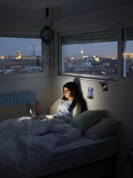 Ein Mädchen liegt zur Dämmerung in ihrem Bett und schaut auf ihren Laptop.