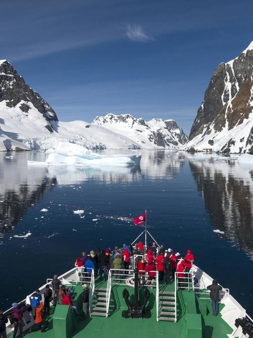 Besucher auf dem Bug des Expeditionskreuzfahrtschiffs MS Expedition betrachten sich spiegelnde Szenerie des Lemaire-Kanals auf der Antarktischen Halbinsel