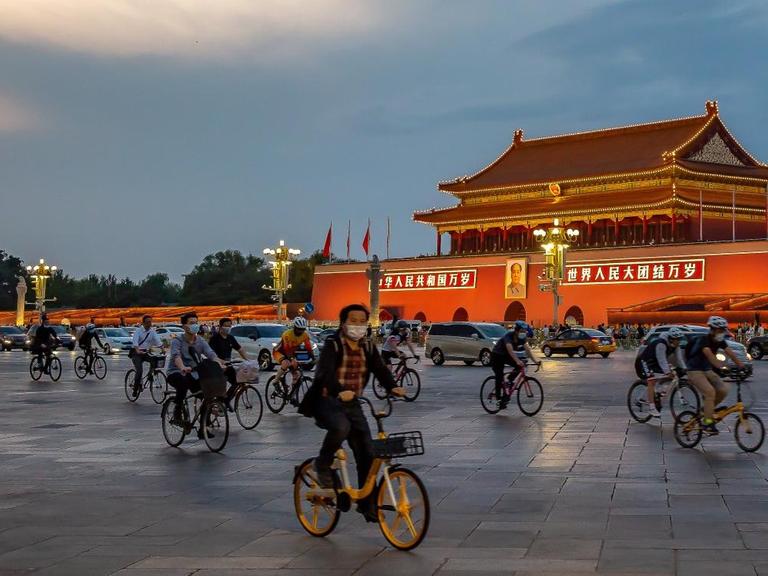 Das tägliche Leben in Peking: Fahrradfahrer und Autos auf dem erleuchteten Tian’anmen-Platz in Peking, China.