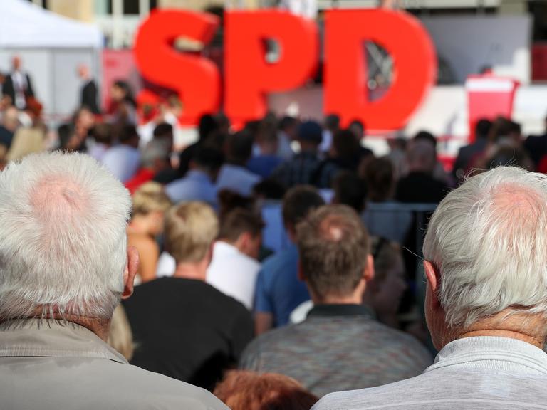 Zwei grauhaarige Männer verfolgen eine Wahlkampfveranstaltung der SPD am 2017 auf dem Nikolaikirchhof in Leipzig, auf der Bühne stehen die drei großen roten Buchstanden "SPD"