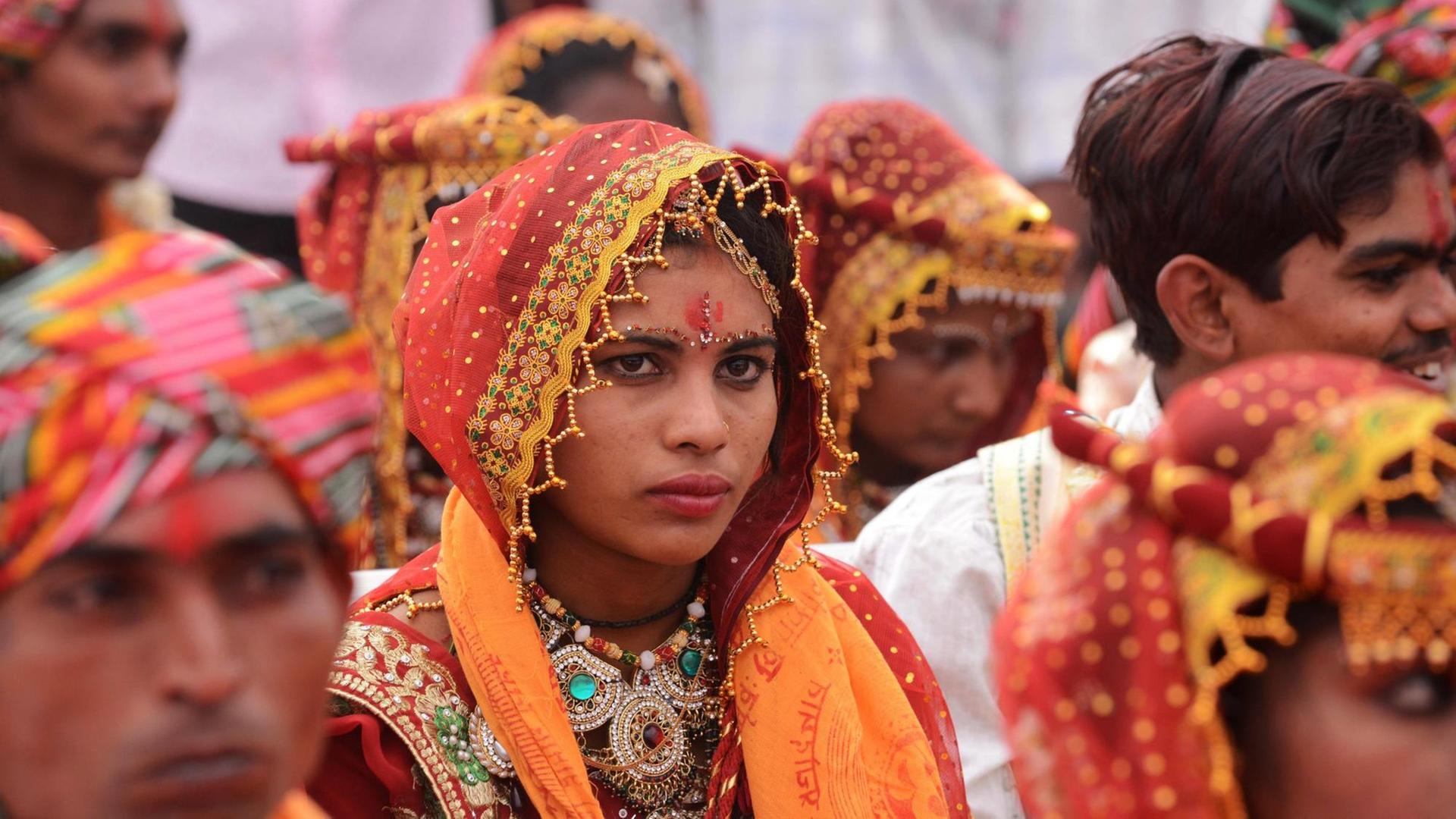 Eine junge indische Braut steht während einer Massenhochzeit zwischen anderen Frauen und Männern.