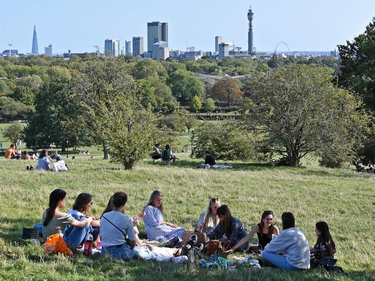 Freunde sitzen für ein Picknick im Kreis in einem Park.