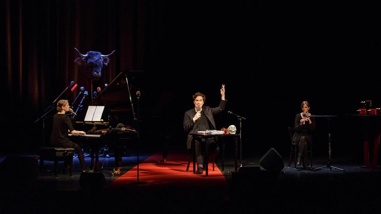 Der Kabarettist Hosea Ratschiller auf der Bühne des Stadttheaters Schaffhausen beim Salzburger Stier 2017. Links und rechts von ihm Birgit und Nicole Radeschnig, die ihn musikalisch mit Klavier und Blockflöte begleiten.