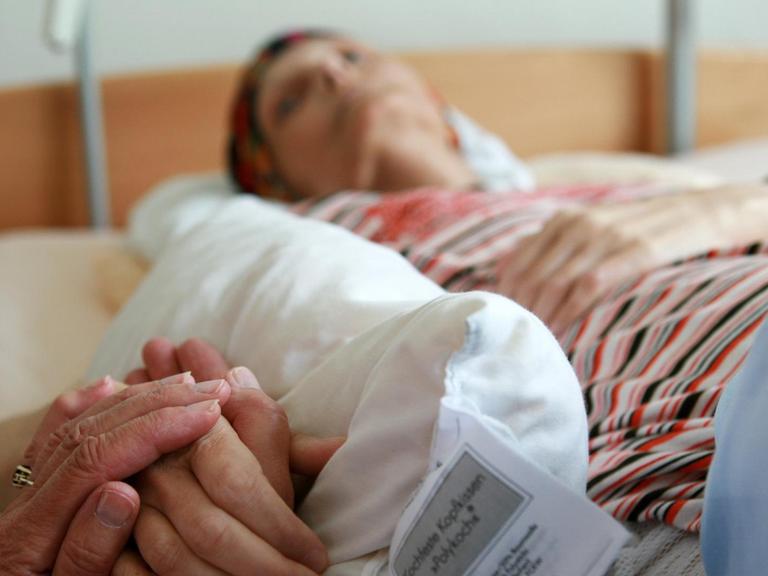 Eine ehrenamtliche Helferin hält die Hand einer sterbenden Bewohnerin, die in ihrem Bett im Christophorus Hospiz in München liegt
