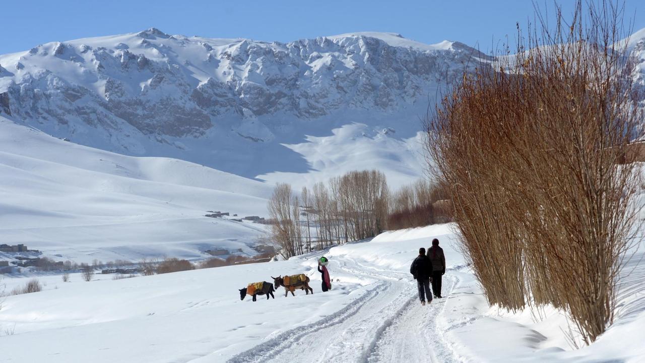 Menschen laufen mit ihren Tieren durch eine verschneite Landschaft im Bamiyan-Tal, Afghanistan
