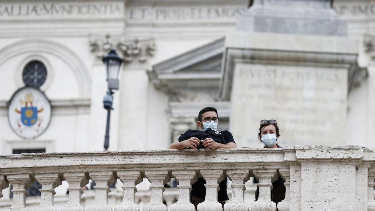 Rom: Menschen mit Mund-Nasen-Schutz stehen an einem Zaun. 