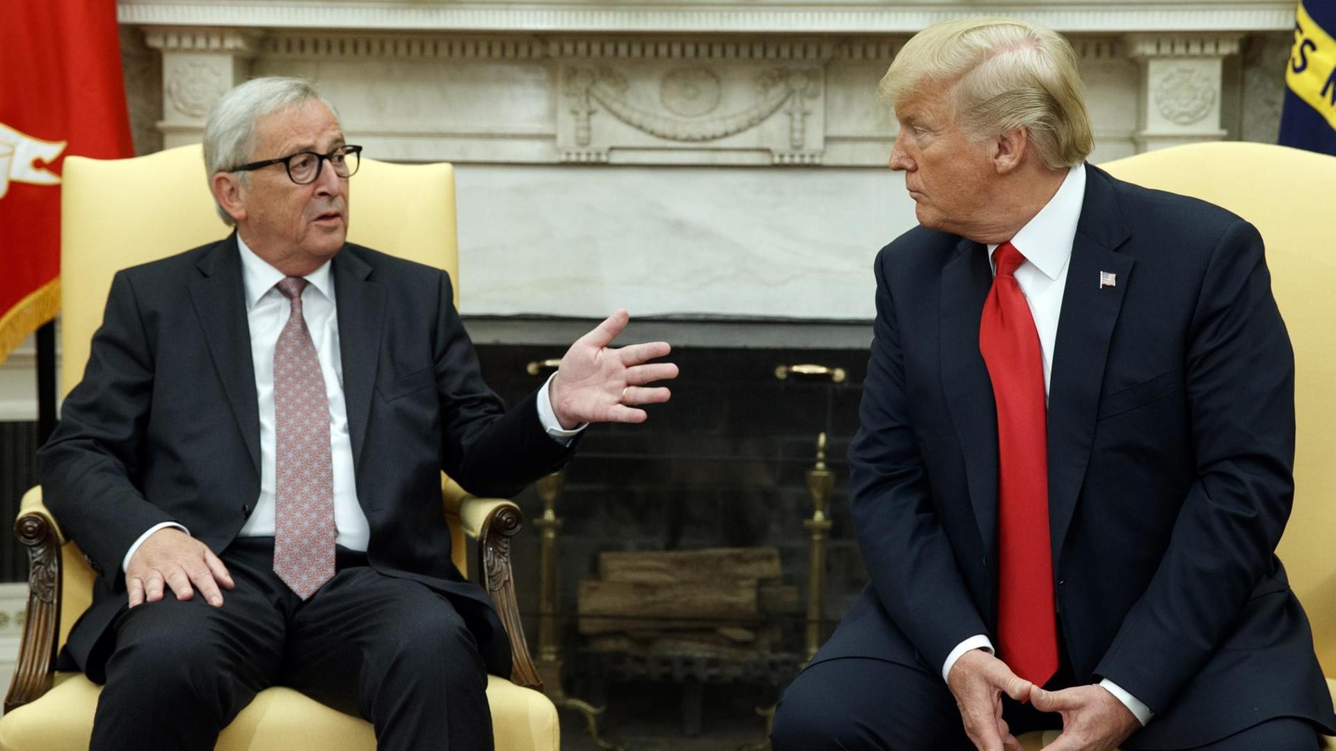 Das Bild zeigt EU-Kommissionspräsident Jean-Claude Juncker (l.), wie er im Weißen Haus von US-Präsident Donald Trump empfangen wird. Beide sitzen auf heöö bezogenen Stühlen nebeneinander vor einem Kamin und unterhalten sich miteinander. Beide machen ernste Gesichter.