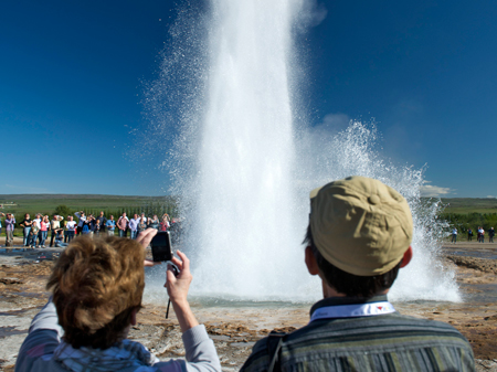 Touristen stehen um die Wasserfontäne eines Geysirs
