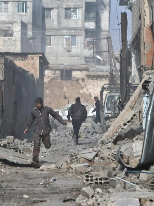 Syrische Männer rennen durch eine Straße in Ost-Ghouta, die von Trümmern gesäumt ist.