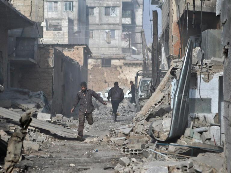 Syrische Männer rennen durch eine Straße in Ost-Ghouta, die von Trümmern gesäumt ist.
