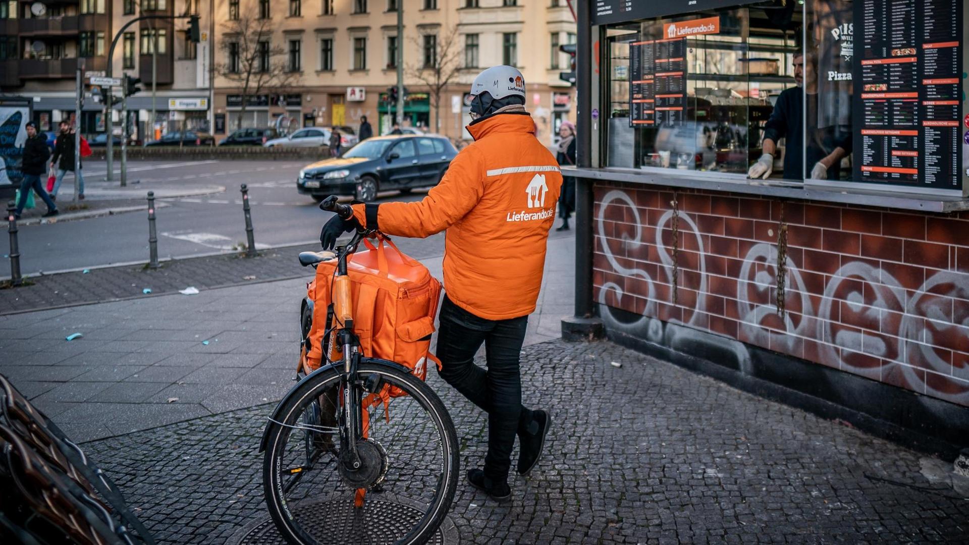 Ein Fahrrad Kurier des Online Essens Lieferservice "Lieferando" wartet an einem Kiosk in Kreuzberg auf neue Aufträge.