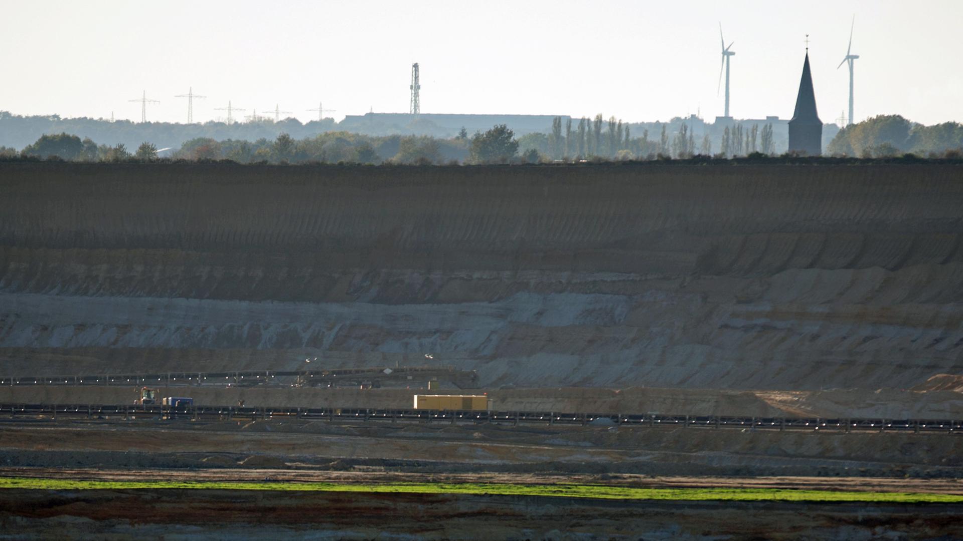 Tiefe Senke des Braunkohletagebaus "Garzweiler 2" bei Holz in Nordrhein-Westfalen: Der Kirchturm von Keyenberg und Windkraftanlagen sind im Hintergrund zu sehen; Aufnahme vom Oktober 2014