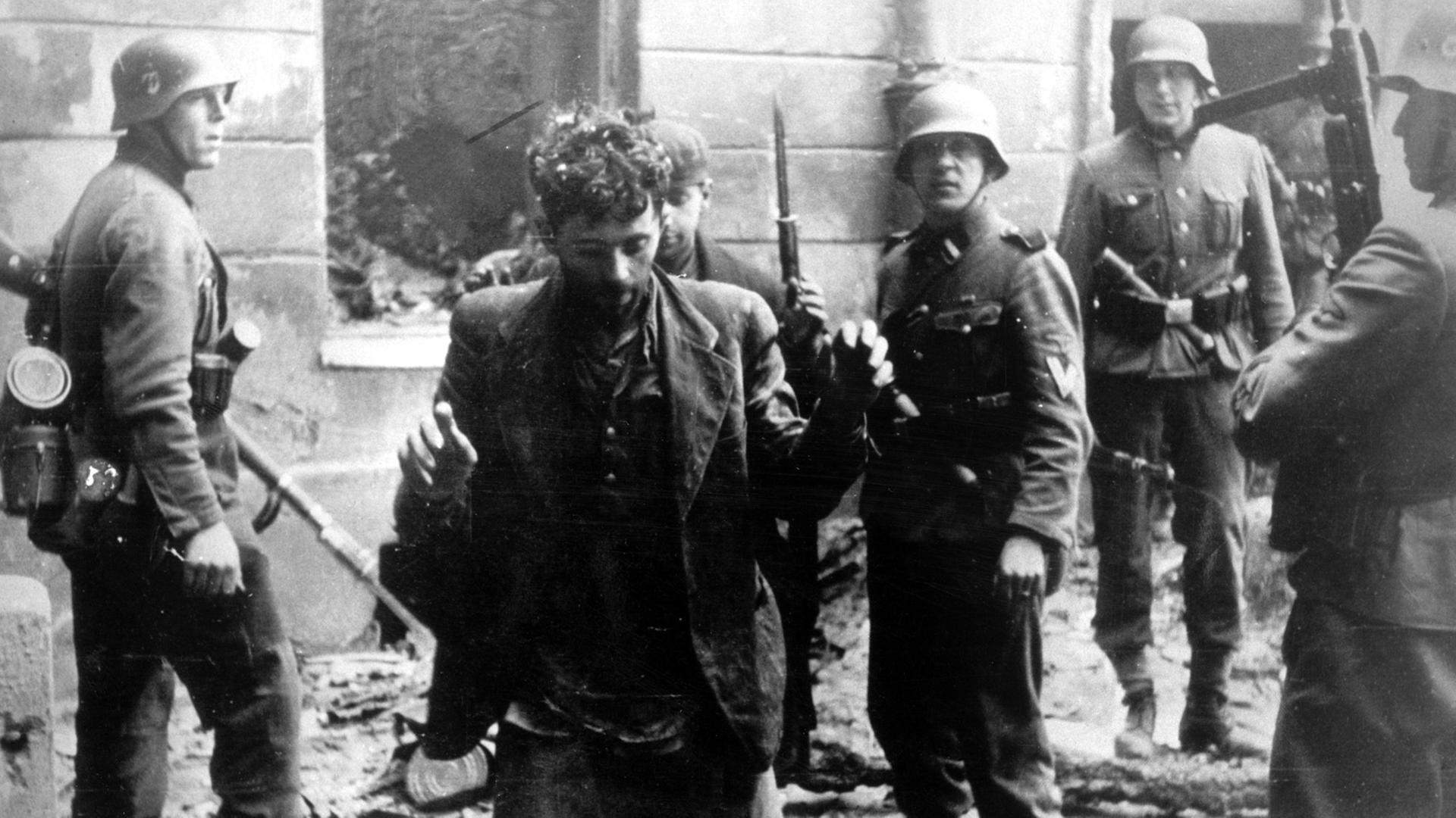 Zwei Juden, die sich in einem Haus versteckt hatten, werden von SS-Soldaten gefangen genommen. Die Aufnahme entstand während des Warschauer Getto-Aufstands, der vom 19. April 1943 bis zu seiner blutigen Niederschlagung am 16. Mai 1943 dauerte. 