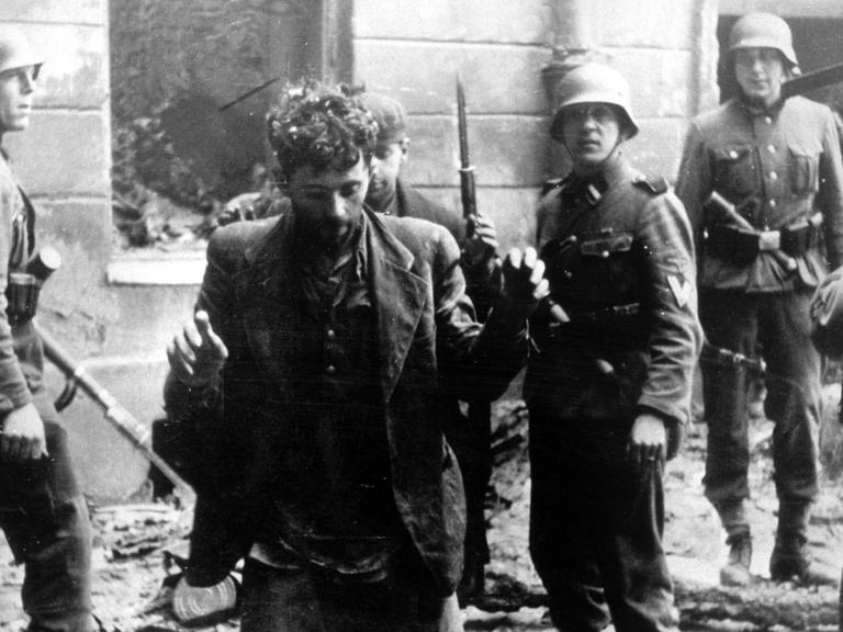 Zwei Juden, die sich in einem Haus versteckt hatten, werden von SS-Soldaten gefangen genommen. Die Aufnahme entstand während des Warschauer Getto-Aufstands, der vom 19. April 1943 bis zu seiner blutigen Niederschlagung am 16. Mai 1943 dauerte. 