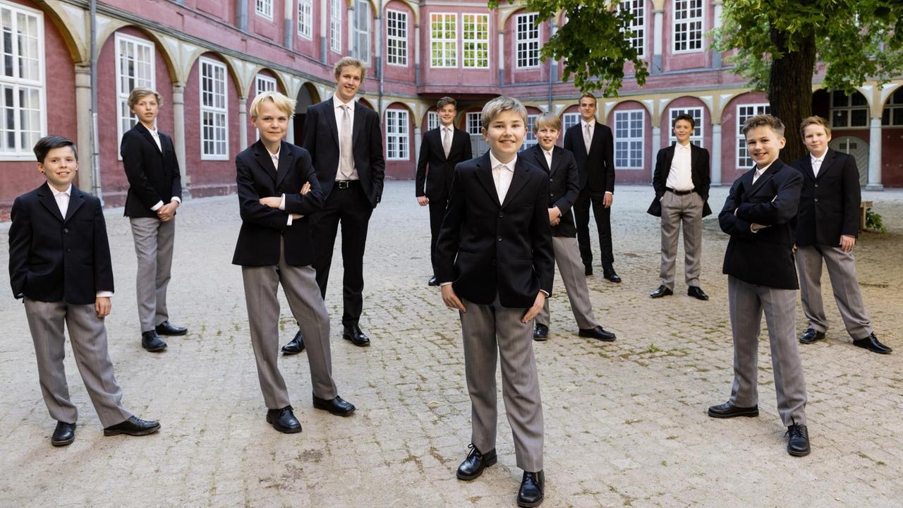 Der Knabenchor Hannover steht in einem historischem Innenhof. Die jungen Männer tragen Anzug und lächeln selbstbewusst in die Kamera.