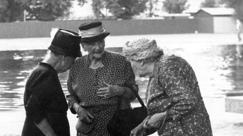 Drei ältere Damen mit Hüten bei einem angeregten Gespräch im Schatten der Schlossgarten-Anlagen in Stuttgart. Aufnahme von 1955.