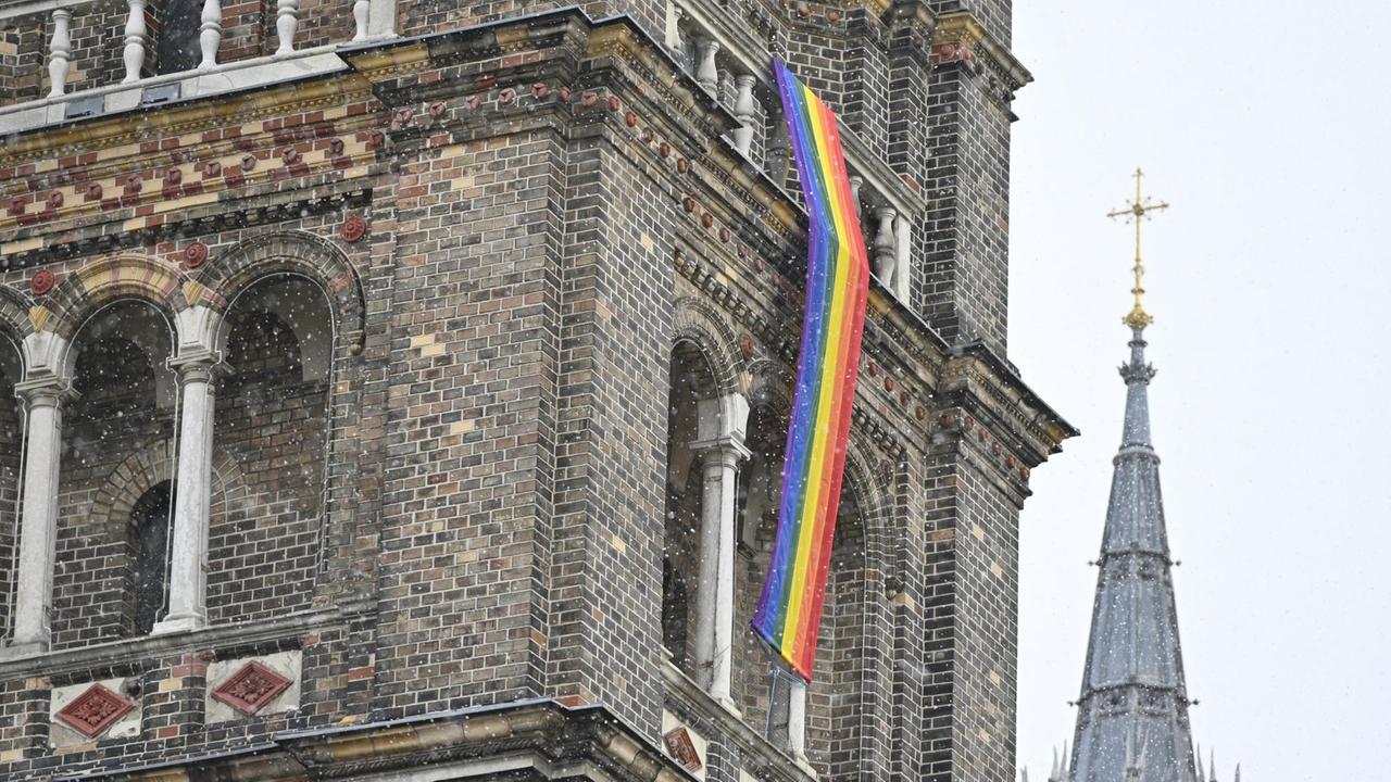 Eine Regenbogenfahne schmückt eine Kirche. 