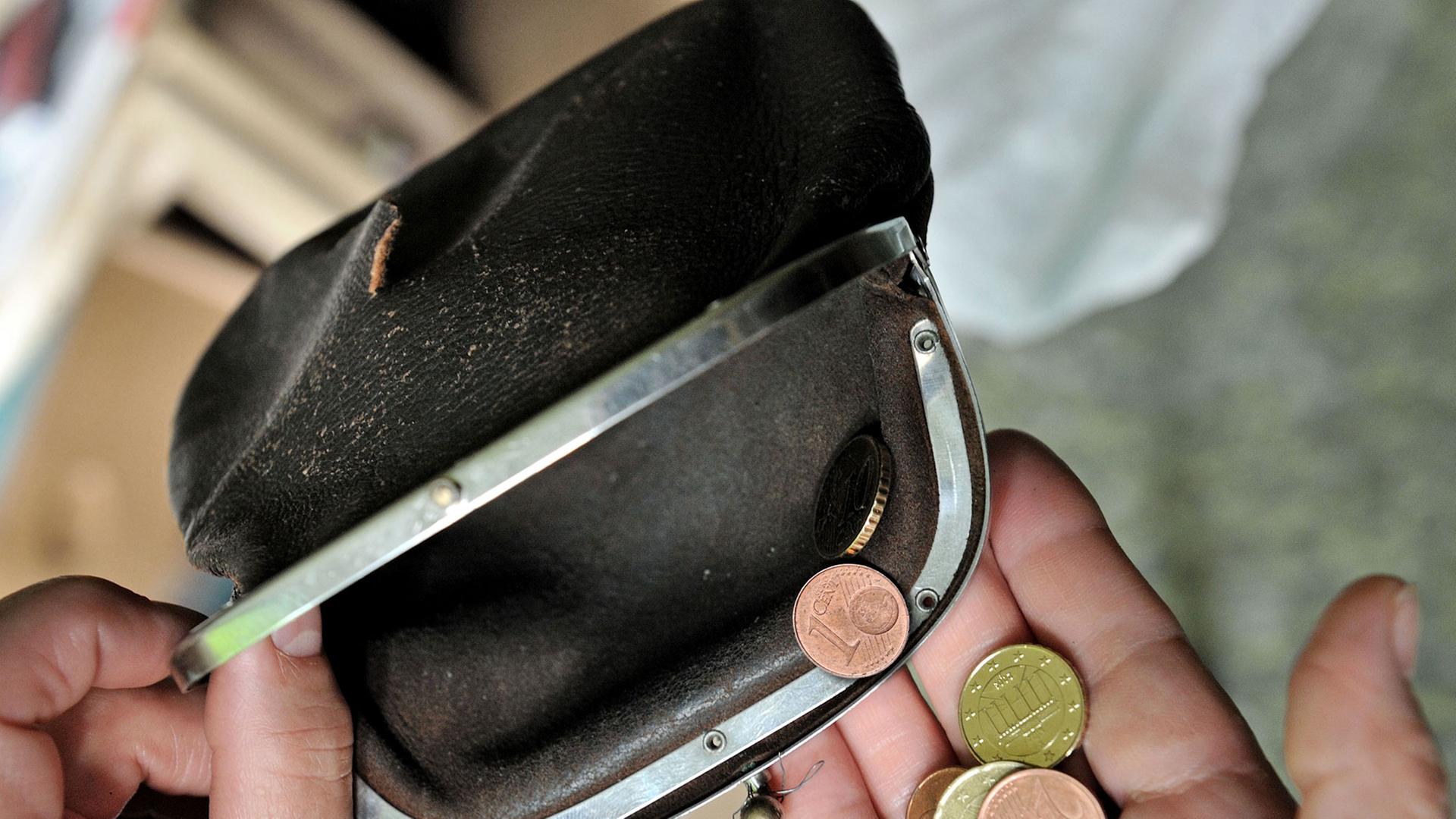 Ein paar Münzen in einer Hand vor einem geöffneten Portemonnaie