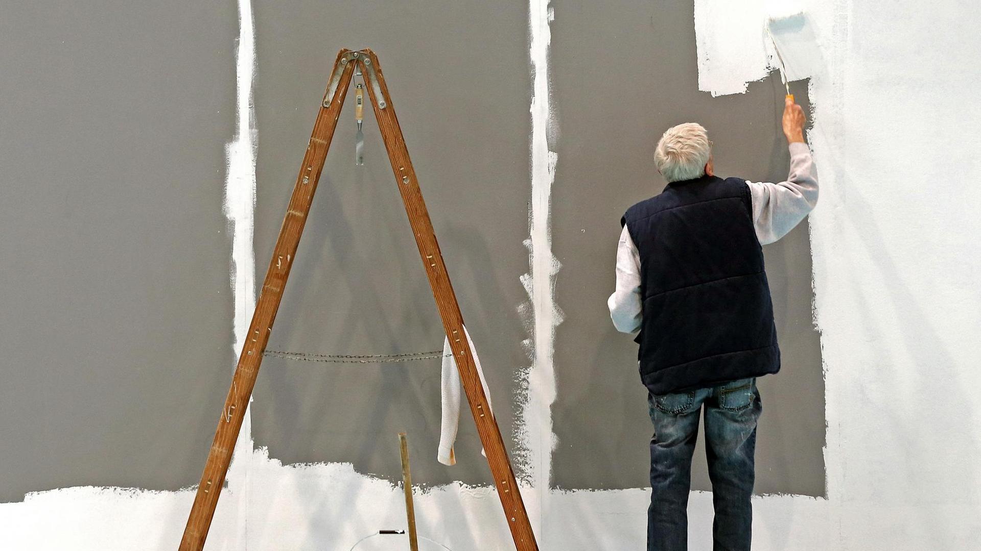 Ein älterer Mann streicht eine Wand.