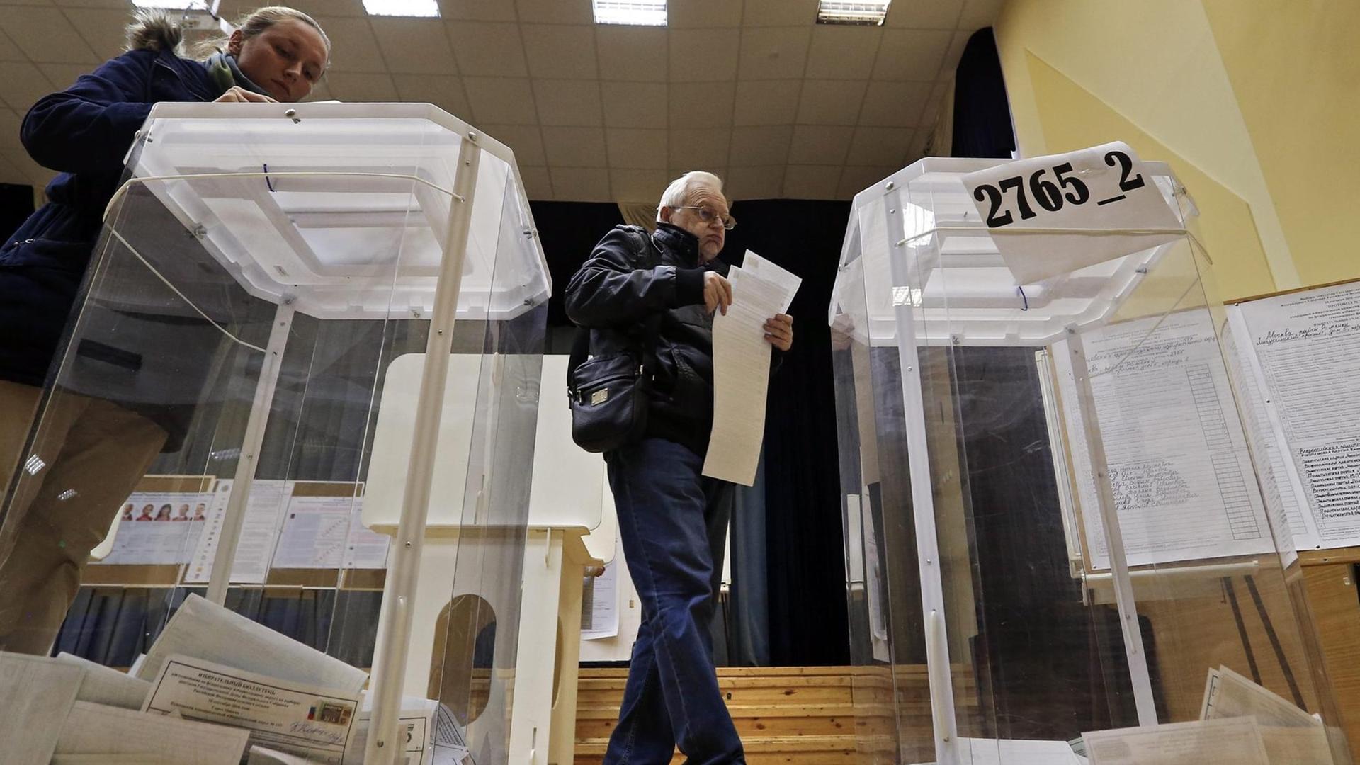 Zwei durchsichtige Wahlurnen stehen auf dem Boden. Dazwischen ein Mann, der seinen Wahlzettel einwirft.