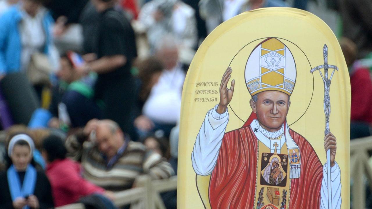 Menschen halten ein Bild von Papst bei dessen Heiligsprechung auf dem Petersplatz in die Höhe.