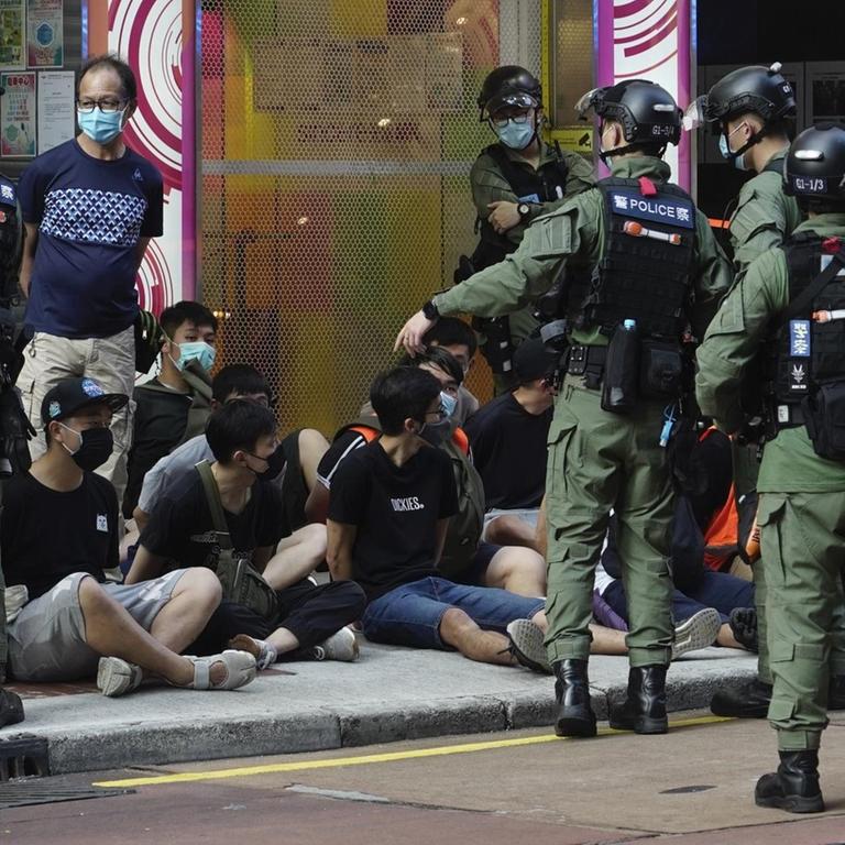 Polizisten in Hongkong nehmen Demonstranten fest, die auf dem Bürgersteig sitzen.