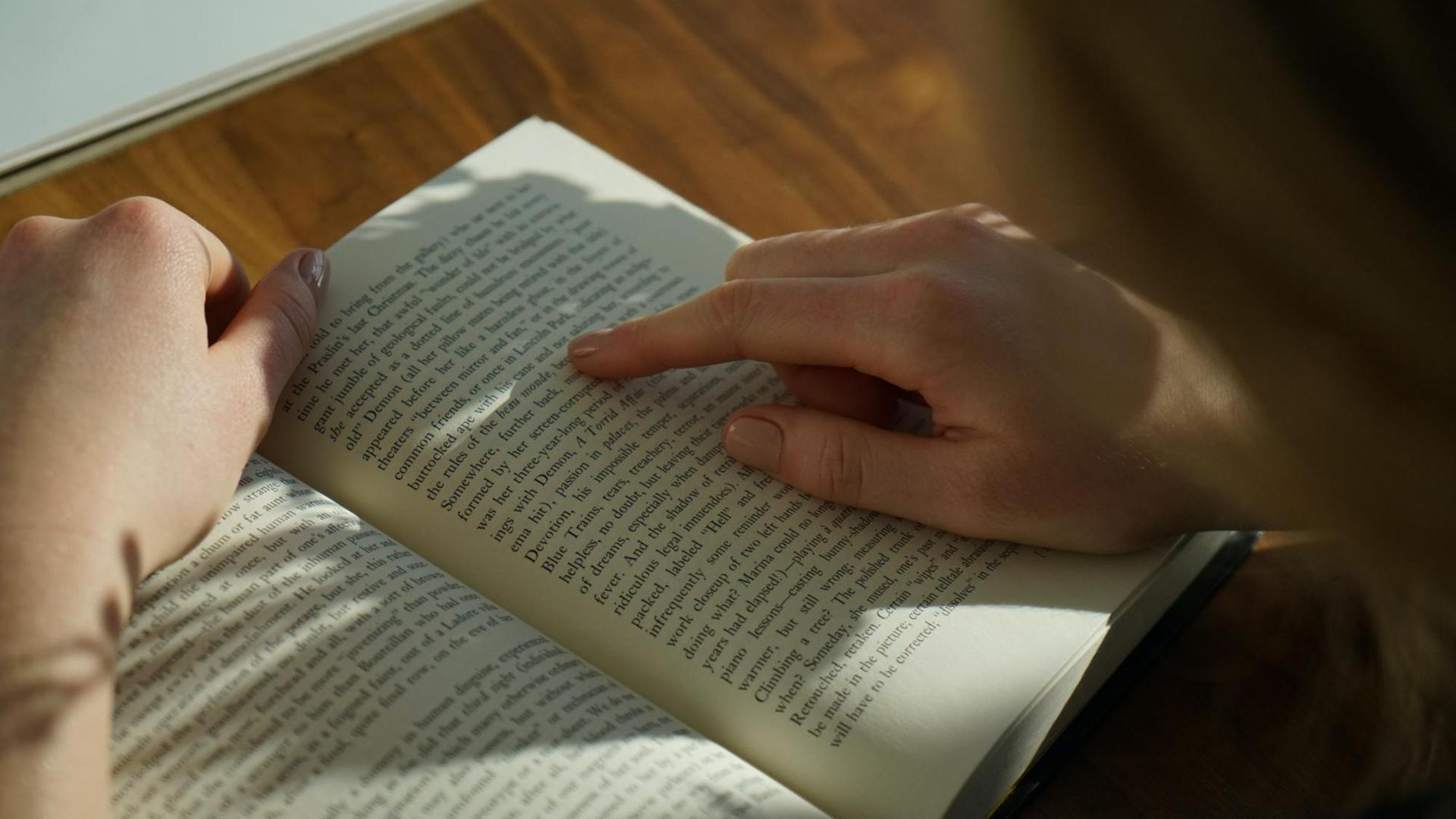 Eine Hand fährt mit dem Zeigefinger die Zeilen eines aufgeschlagenen Buches nach.