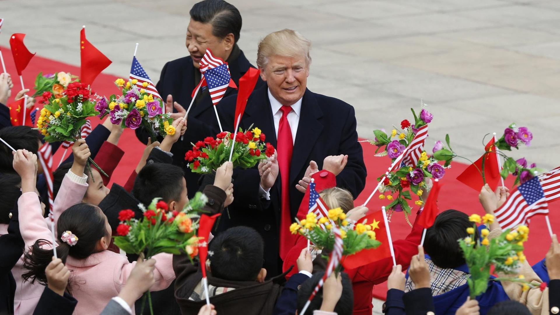 Donald Trump (r.) und Xi Jinping werden von Blumen und Flaggen schwenkenden Kindern begrüßt.