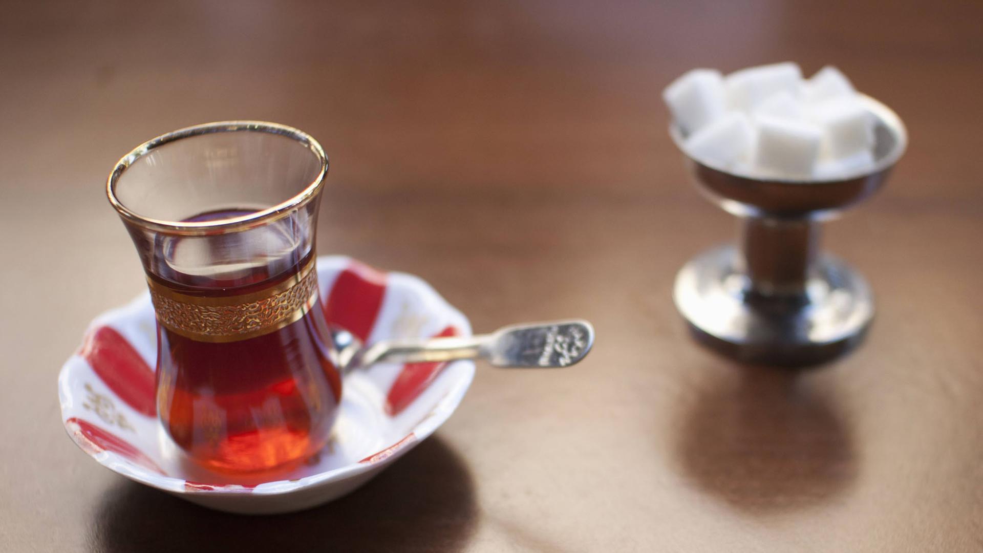 Eine kleines Glas Tee steht mit Würfelzucker auf einem Tisch.