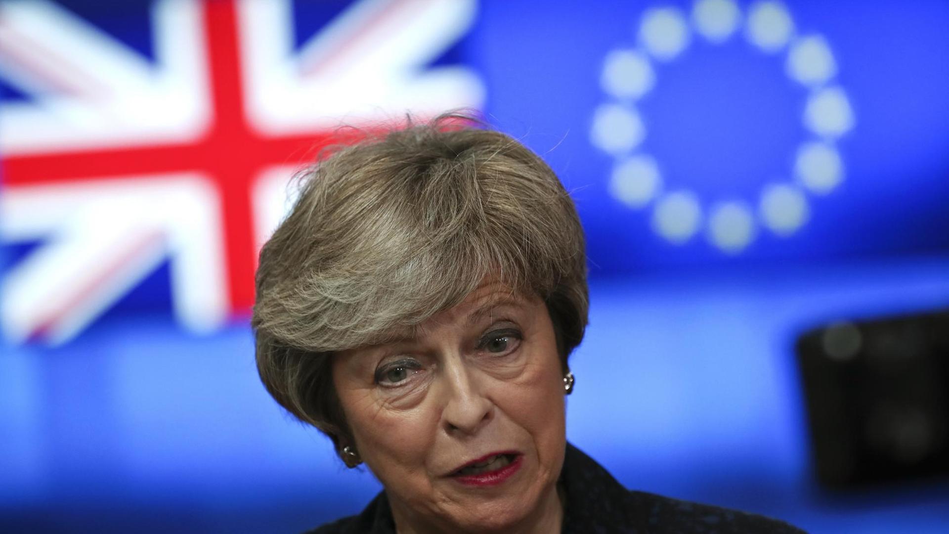 Theresa May, Premierministerin von Großbritannien, steht vor einem Bildschirm mit den Flaggen Großbritanniens und der EU.