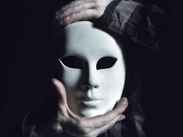 Die Hände eines Mannes halten eine weisse Maske.