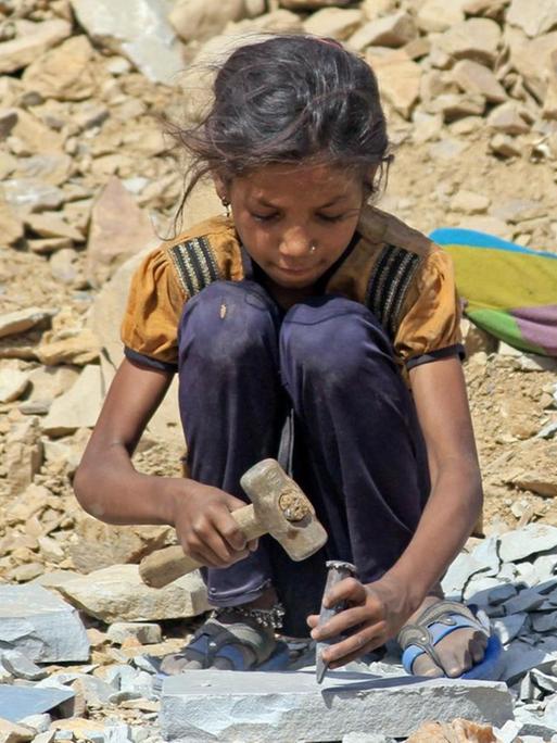 Das Foto zeigt ein Mädchen in einem indischen Steinbruch, das Steine zerklopft.