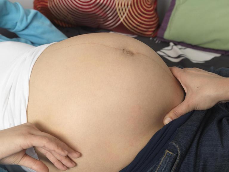 Nahaufnahme einer schwangeren Frau, die von einer Hebamme untersucht wird.