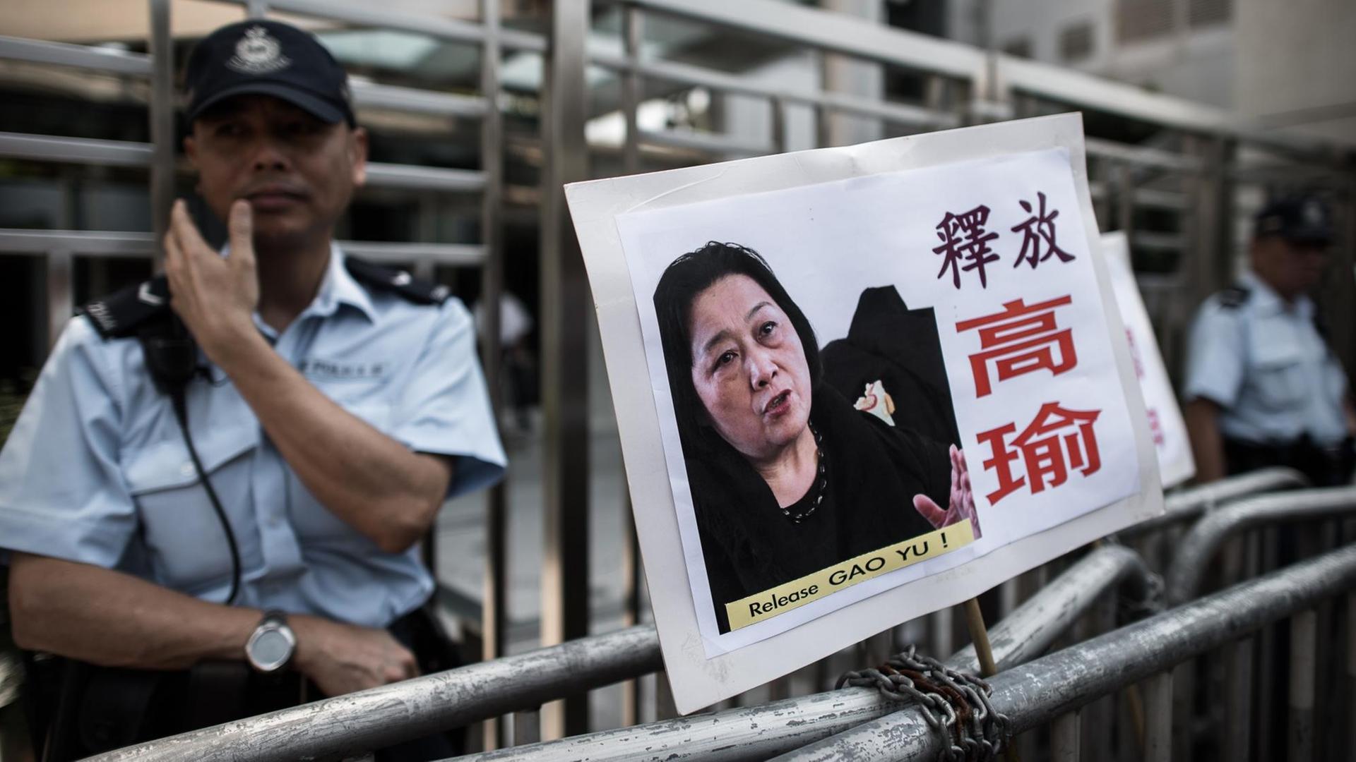 Ein Polizist steht in Hong Kong neben einem Schild mit einem Bild von Gao Yu, das Demonstranten an eine Absperrung gehängt haben