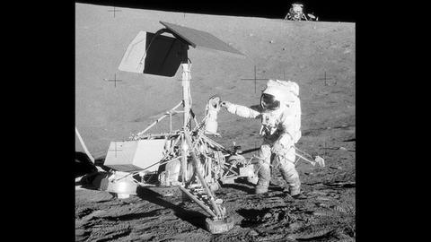 Der "Apollo-12"-Astronaut Charles Conrad inspiziert die ein paar Jahre zuvor auf dem Mond gelandete Raumsonde Surveyor-3; im Hintergrund die Landefähre Intrepid.