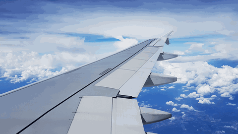 Hörstück zum Luftverkehr. Die Tragfläche eines Flugzeuges im Flug mit blauem Himmel mit weißen Wolken sind zu sehen.  