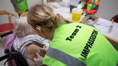 Die Mitarbeiterin eines mobilen Impfteams klebt im Alten- und Pflegeheim Bürgerheim nach einer Impfung mit dem Corona-Impfstoff von Biontech/Pfizer bei einer Bewohnerin ein Pflaster auf den Arm.