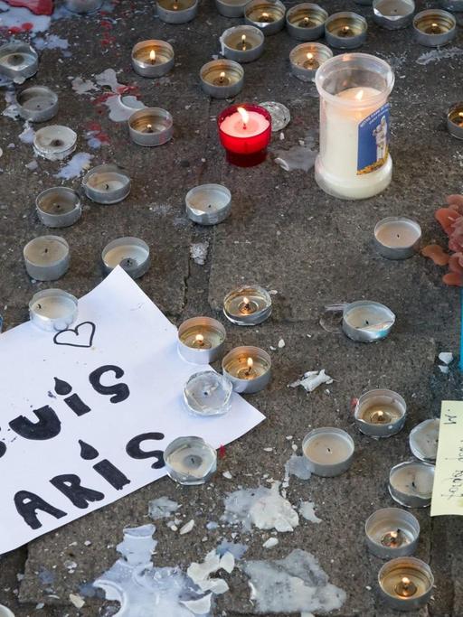 Zu sehen sind viele Teelichter, und der Schriftzug "Je suis Paris" auf einem Blatt Papier.