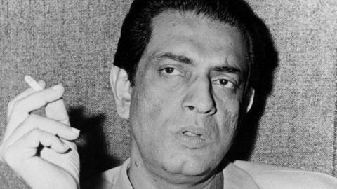 Ein Schwarzweiß-Foto zeigt einen Mann in hellem Anzug in die Kamera blickend. In der erhobenen rechte Hand hält er eine Zigarette Der indische Regisseur des bengalischen Films und Oscar-Preisträger Satyajit Ray
