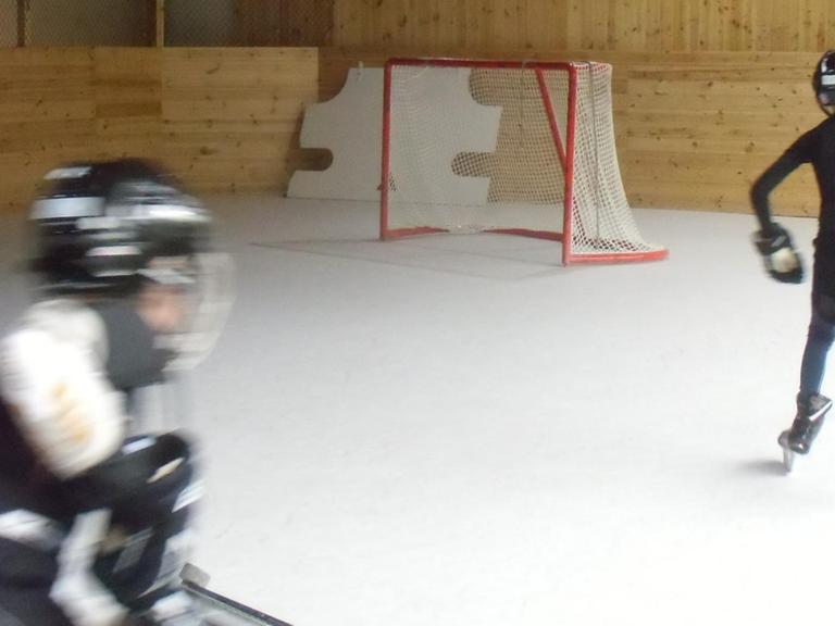 Zwei Kinder trainieren in einer Eishockey Halle auf Polyethylen-Boden mangels Eiszeiten.