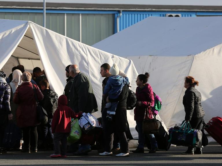 Flüchtlinge stehen in einer Schlange vor einem weißen Zelt an.