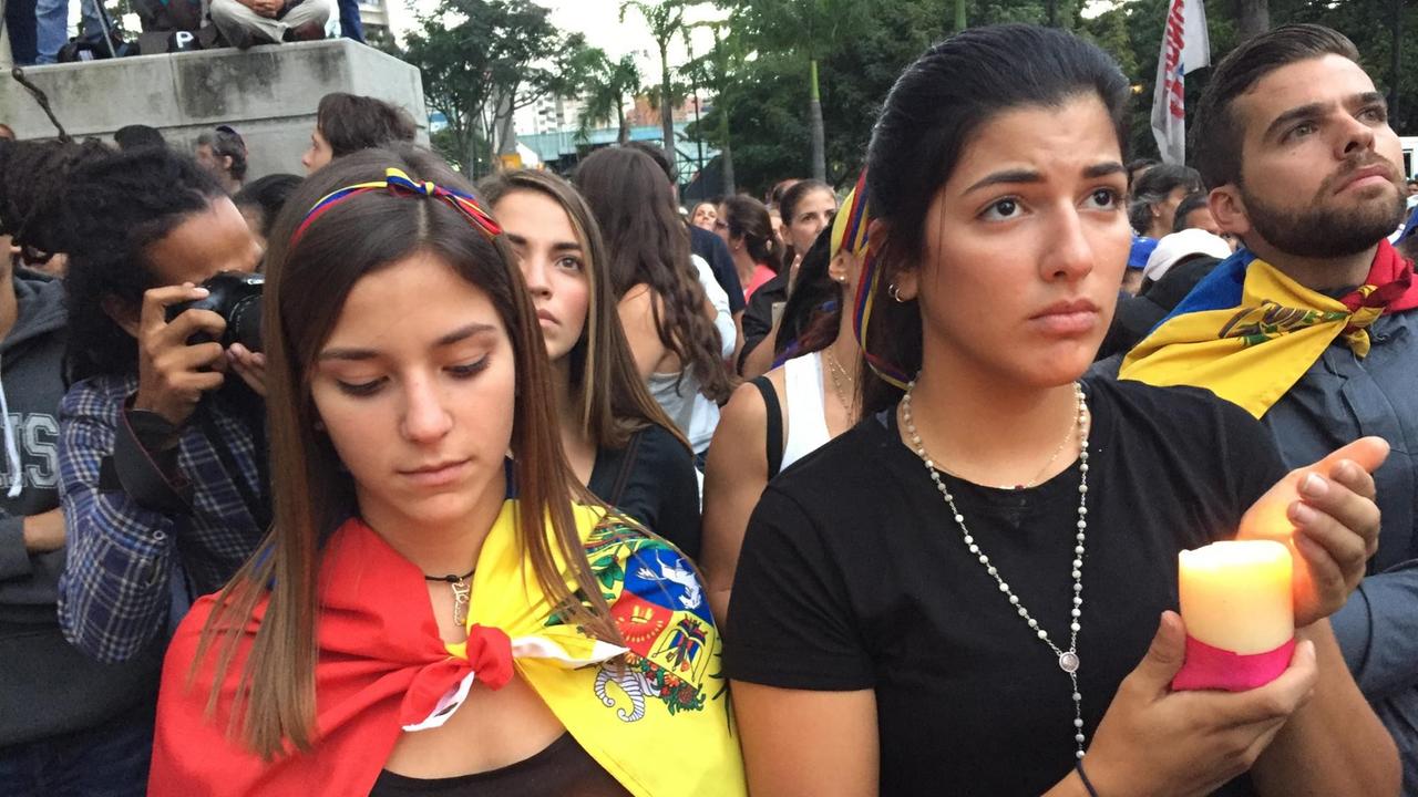 Zwei Frauen aus Venezuela halten Kerzen in den Händen und trauern.