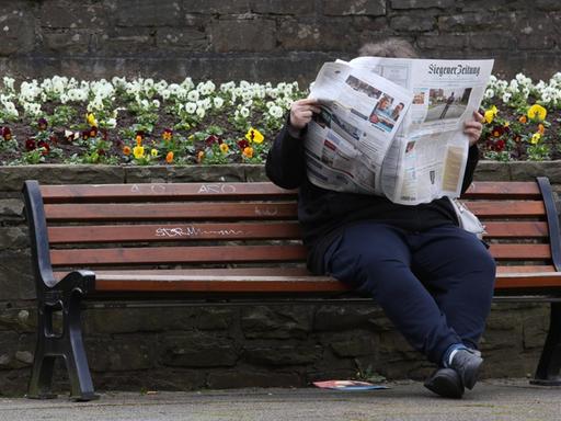 Eine Frau sitzt auf einer Bank und liest die "Siegener Zeitung".